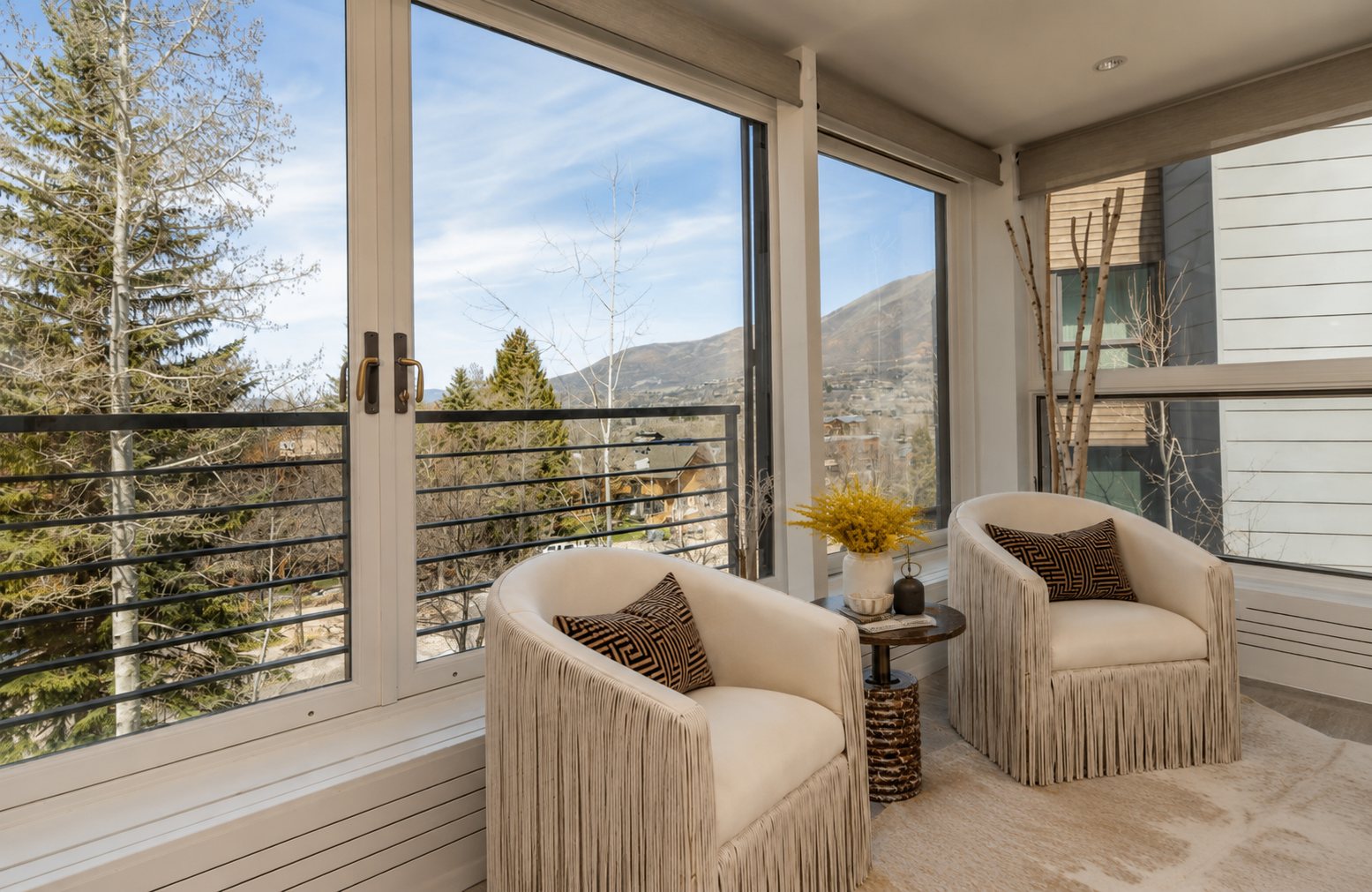 Fringed chairs at a corner window with a view of pines