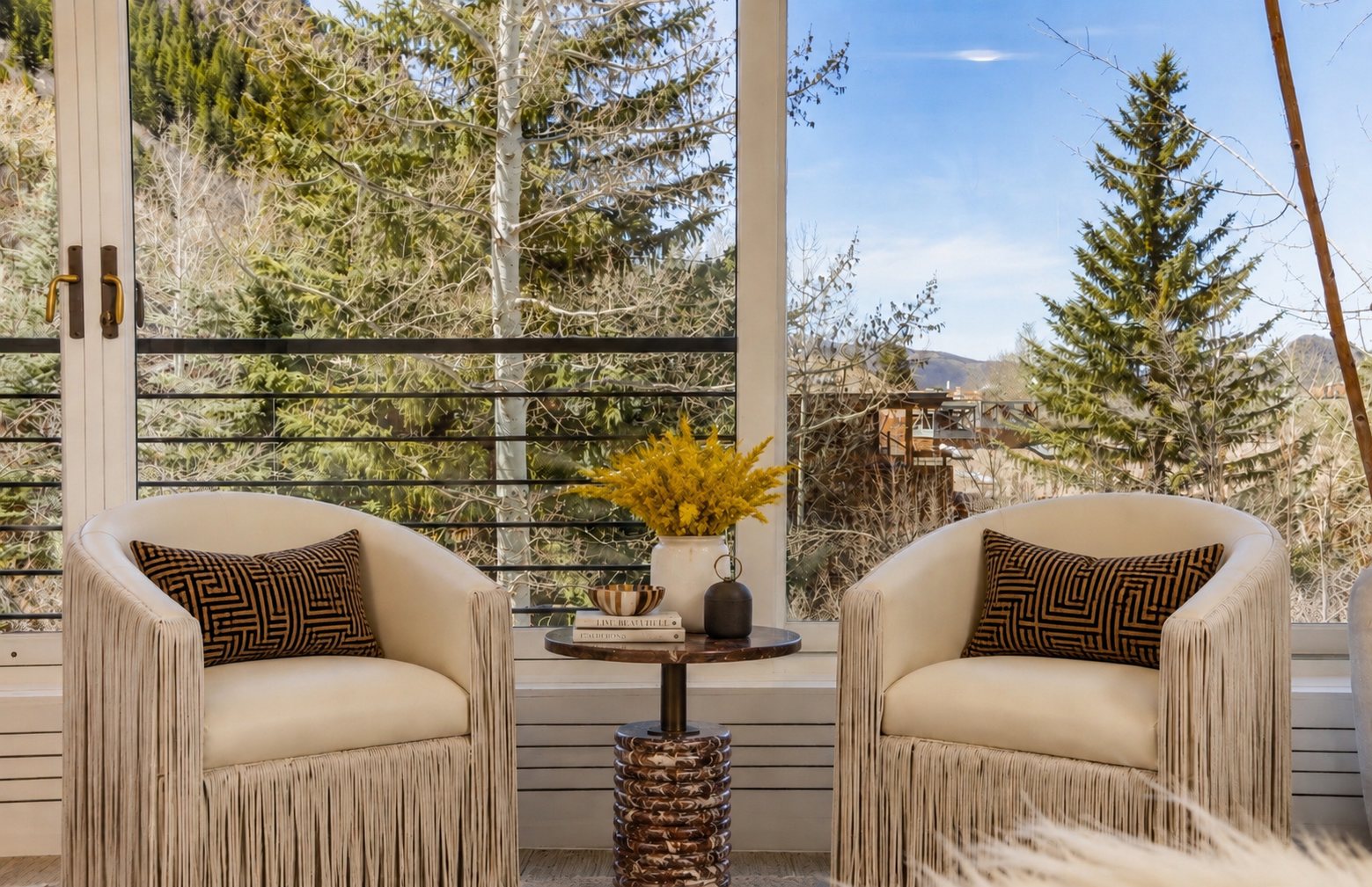 Pair of fringed chairs at a window overlooking pines